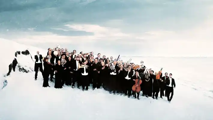 En samling personer i svarta kostymer, några med instrument, står i ett vinterslandskap.