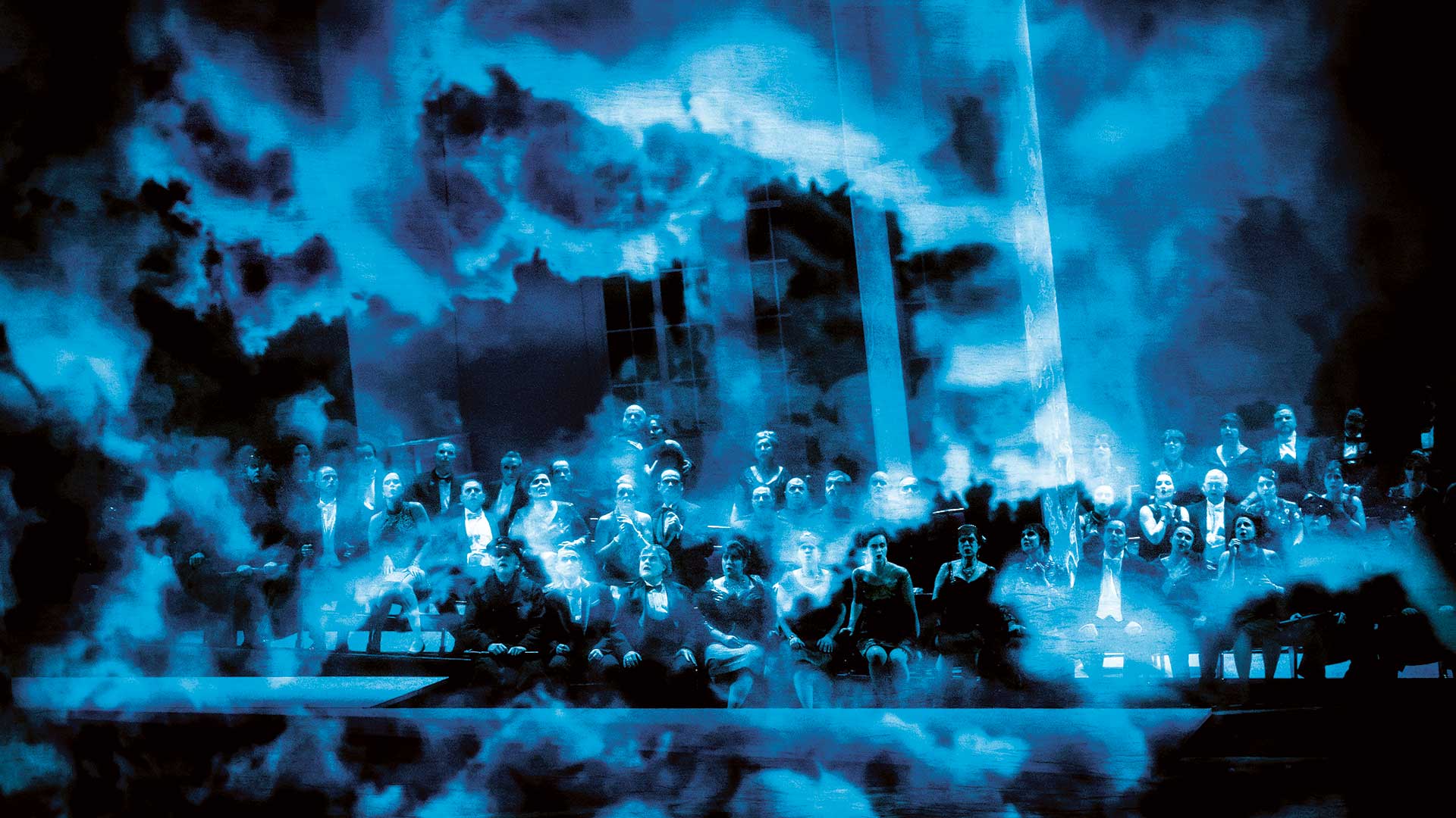 En scen badar i blått ljus och rök, på scenen sitter en stor kör.