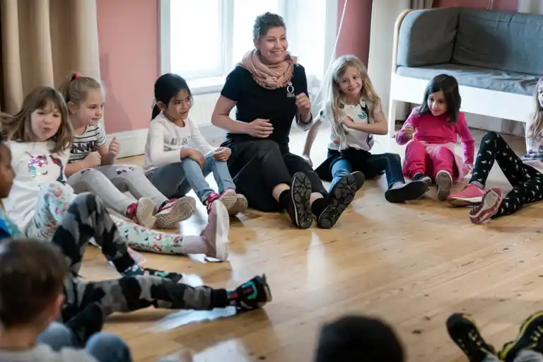 Pedagog med barn i en ring som gör musikaliska övningar.