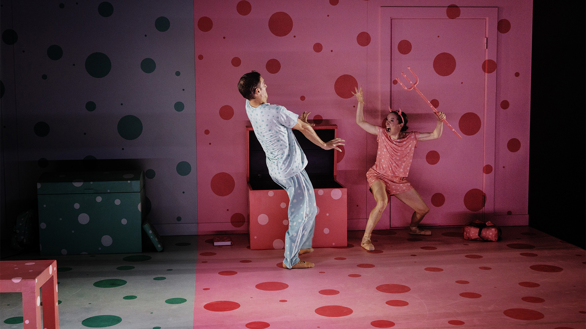 En flicka med en treudd och djävulshorn skrämmer en pojke på en scen.