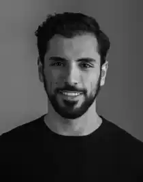 Porträttbild av en leende mörkhårig man med skägg, iklädd en mörk tröja.