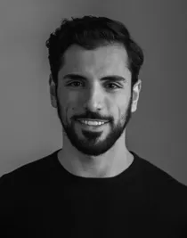 Porträttbild av en leende mörkhårig man med skägg, iklädd en mörk tröja.