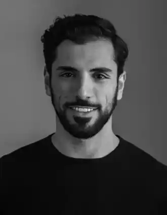 Portrait image of a smiling dark-haired man with a beard, wearing a dark shirt.
