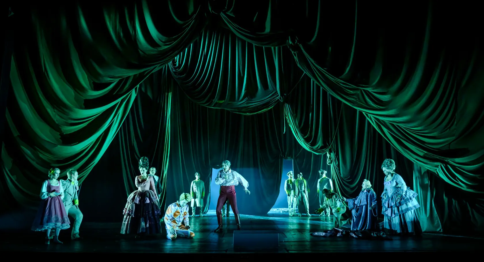 En grupp människor på en scen, omgivna av ett tungt grönt draperi.