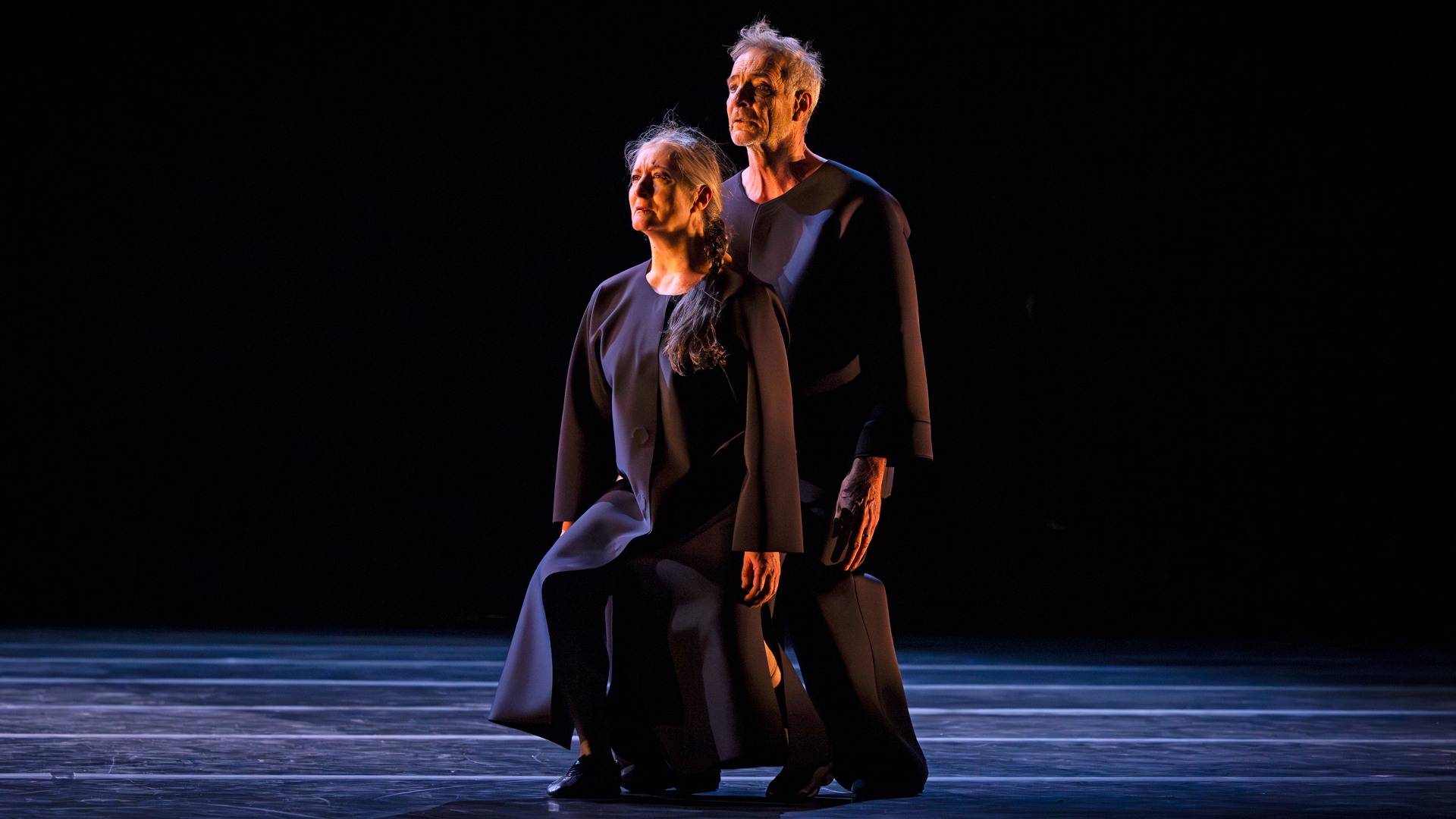 A woman and a man stand with bent knees on a stage.