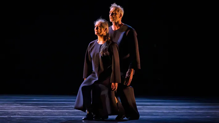 A woman and a man stand with bent knees on a stage.