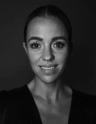 En närbild på en leende kvinna, hennes hår är bakåtstruket och hon bär en mörk urringad topp.