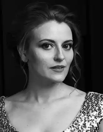 En närbild på en kvinna med uppsatt, lockigt hår, klädd i en topp med paljetter.