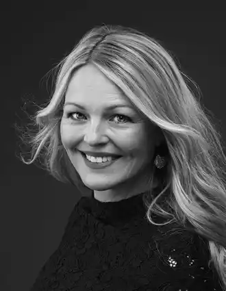 Close-up of blonde woman with bushy hair smiling at camera.