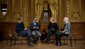 Fyra personer sitter på stolar i ett utsmyckat rum - de verkar samtala med varandra.