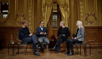 Fyra personer sitter på stolar i ett utsmyckat rum - de verkar samtala med varandra.