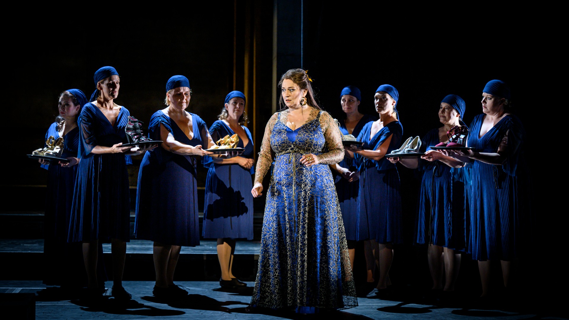 Flera blåklädda damer på en scen, i mitten en kvinna med en guldutsmyckad blå klänning.