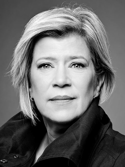 A close-up of a woman with a short blonde hair, her dark collar is turned up.