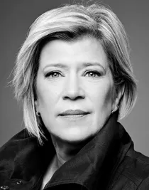 En närbild på en kvinna med kort blont hår, hennes mörka krage är uppfälld.