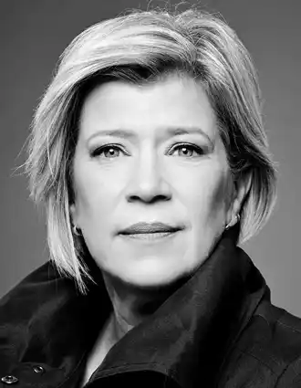 En närbild på en kvinna med kort blont hår, hennes mörka krage är uppfälld.