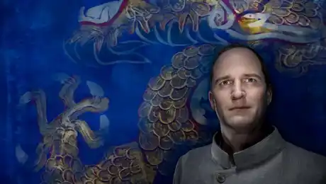 A man stands leaning against a richly decorated blue wall.