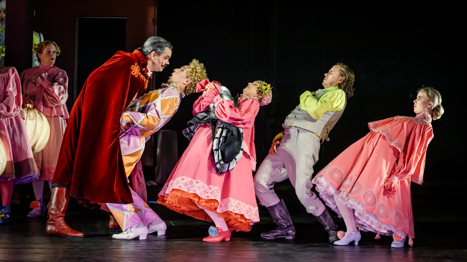 En rödklädd man lutar sig hotfullt framåt mot fyra personer som ryggar tillbaka.