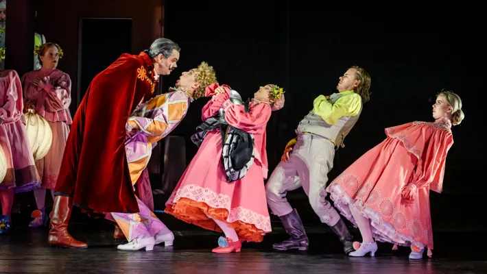 En rödklädd man lutar sig hotfullt framåt mot fyra personer som ryggar tillbaka.