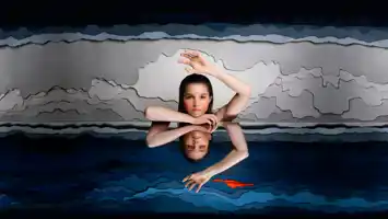A picture of a woman floating on water, she is mirrored in the water.