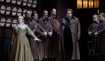 En samling människor står i en köksliknande miljö, tallrikar uppradade på väggen bakom.