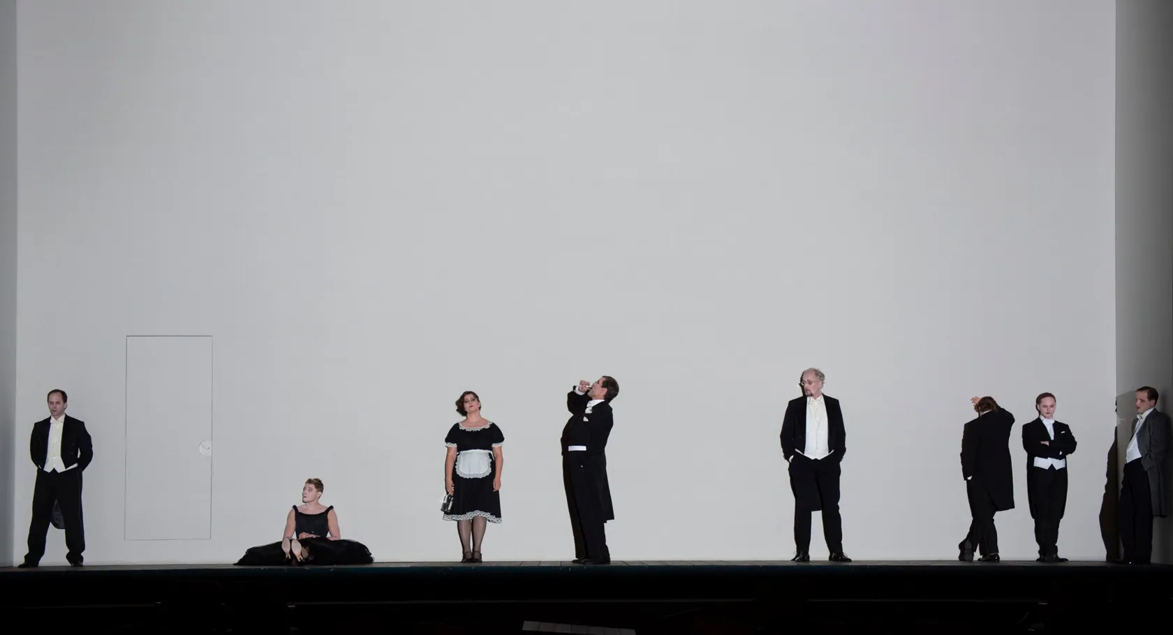 Mot en stor, tom vit vägg står en samling människor klädda i vitt och svart.