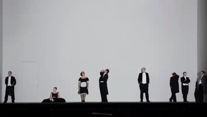Mot en stor, tom vit vägg står en samling människor klädda i vitt och svart.