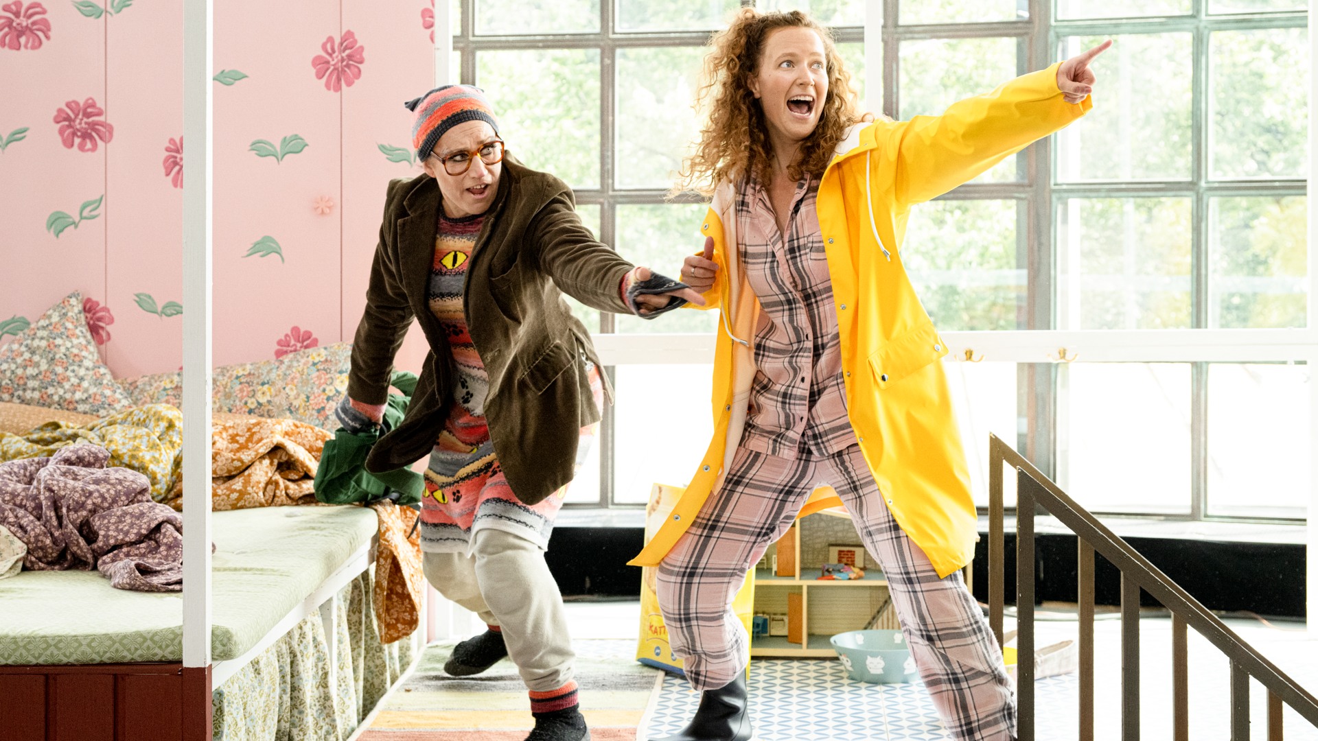 A woman in a yellow raincoat is pointing, she is being held by a person behind her.