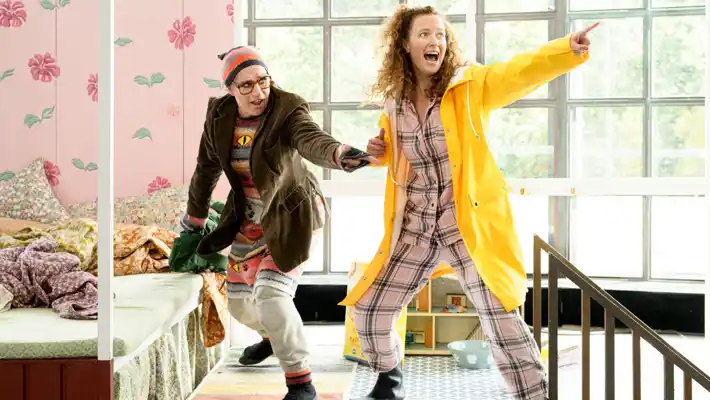 A woman in a yellow raincoat is pointing, she is being held by a person behind her.