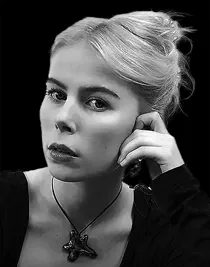 En kvinna med uppsatt hår, lutar sitt ansikte mot handen, bakgrunden är mörk.