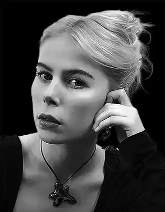 A woman with her hair up, leaning her face against her hand, the background is dark.