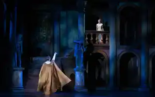 En man med utsträckt arm står nedanför en balkong, på balkongen står en ung kvinna.