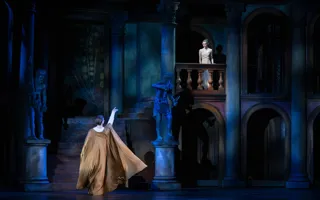 En man med utsträckt arm står nedanför en balkong, på balkongen står en ung kvinna.