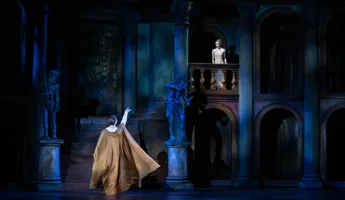 En man med utsträckt arm står nedanför en balkong, på balkongen står en ung kvinna.