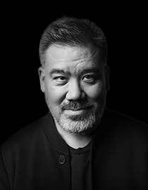 A close-up of a slightly smiling, bearded man dressed in dark clothes.