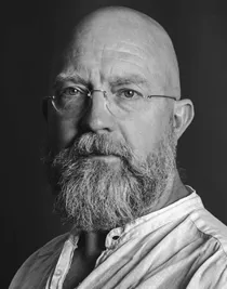 Närbild på en man som bär glasögon, han är klädd i en ljus linneskjorta.