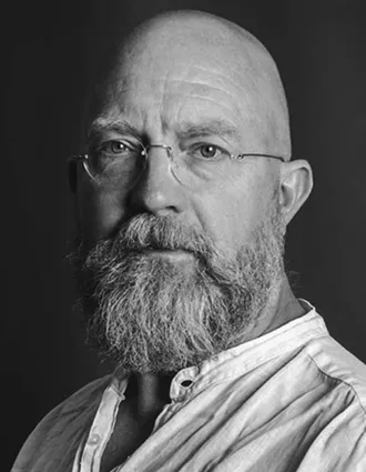 Närbild på en man som bär glasögon, han är klädd i en ljus linneskjorta.