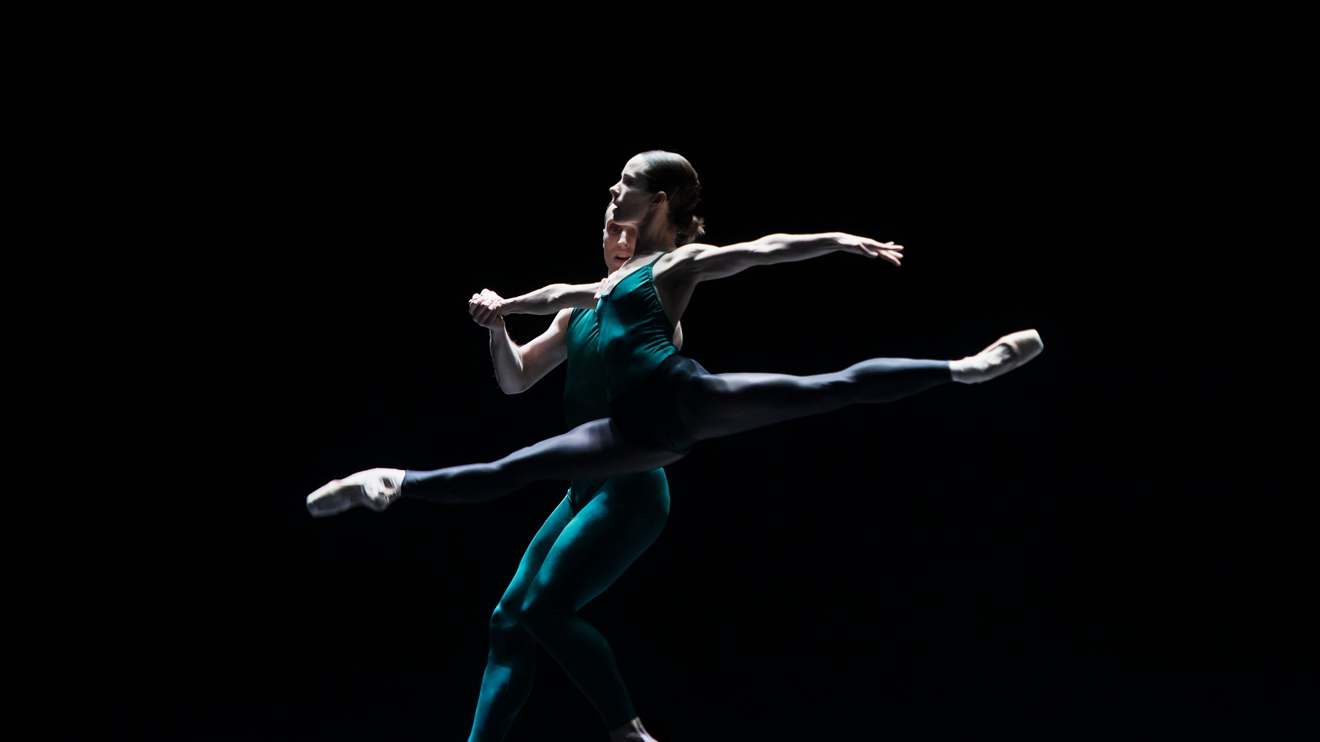 En manlig och en kvinnlig dansare dansar på en mörk scen.