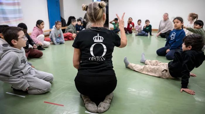 Unga Operan Operaworkshop Barn som sitter i ring på ett golv.